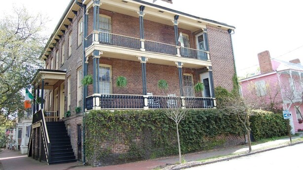 A two-story brick building with a balcony on the second floor, a front entrance with steps, and a flag on the left. - Budget Friendly Apartment on Jones Street! (Savannah)