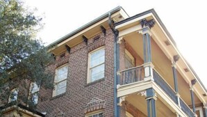 A multi-story brick building with a balcony on the second floor, a staircase leading to the entrance, and a small garden area. - Budget Friendly Apartment on Jones Street! (Savannah)
