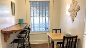 A dining area with a wooden table and chairs, a window with blinds, a small teal bucket, and a wall-mounted decorative piece. - Budget Friendly Apartment on Jones Street! (Savannah)