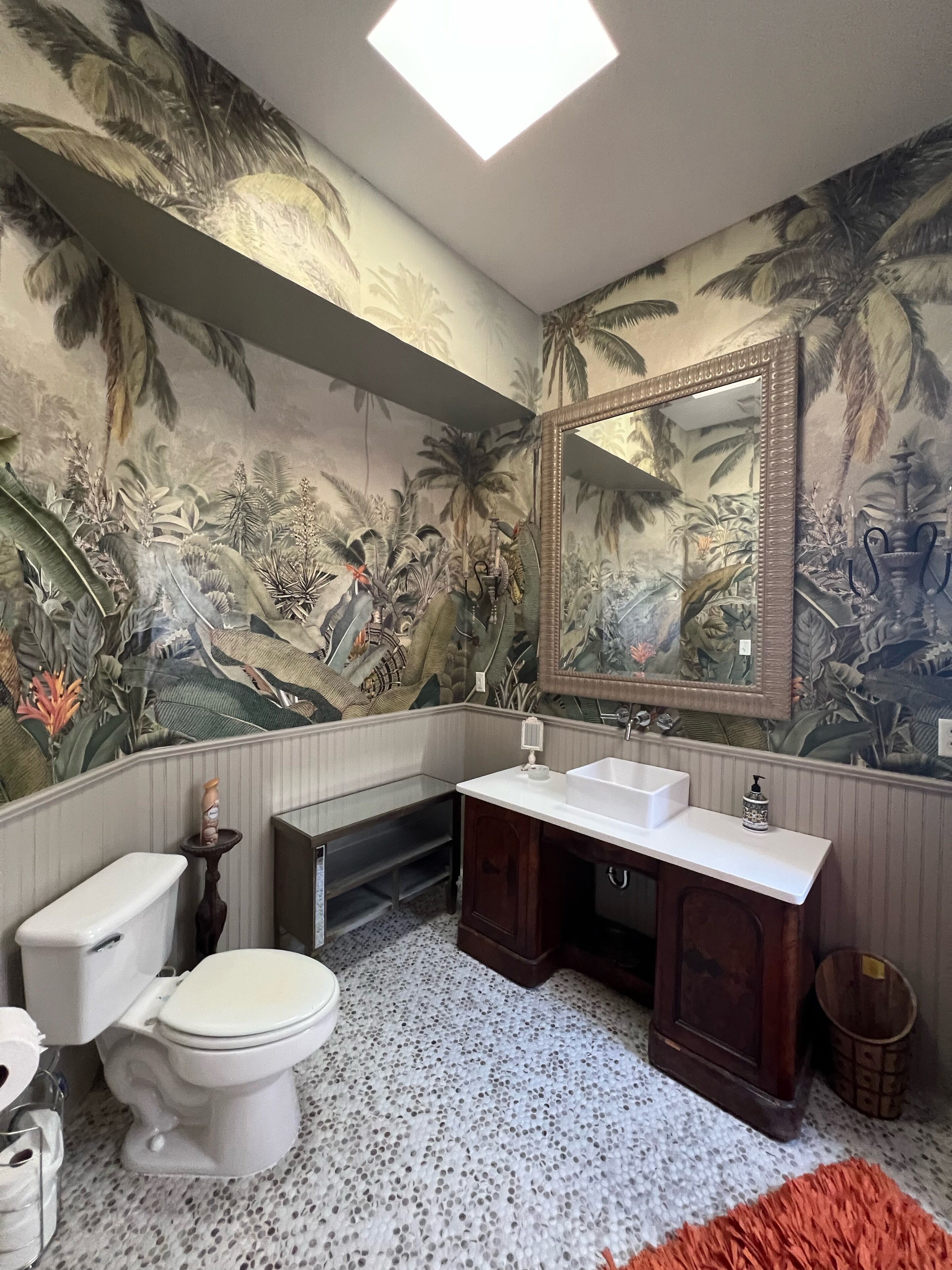 A bathroom with a toilet, sink, and mirror. The walls are decorated with a tropical mural.