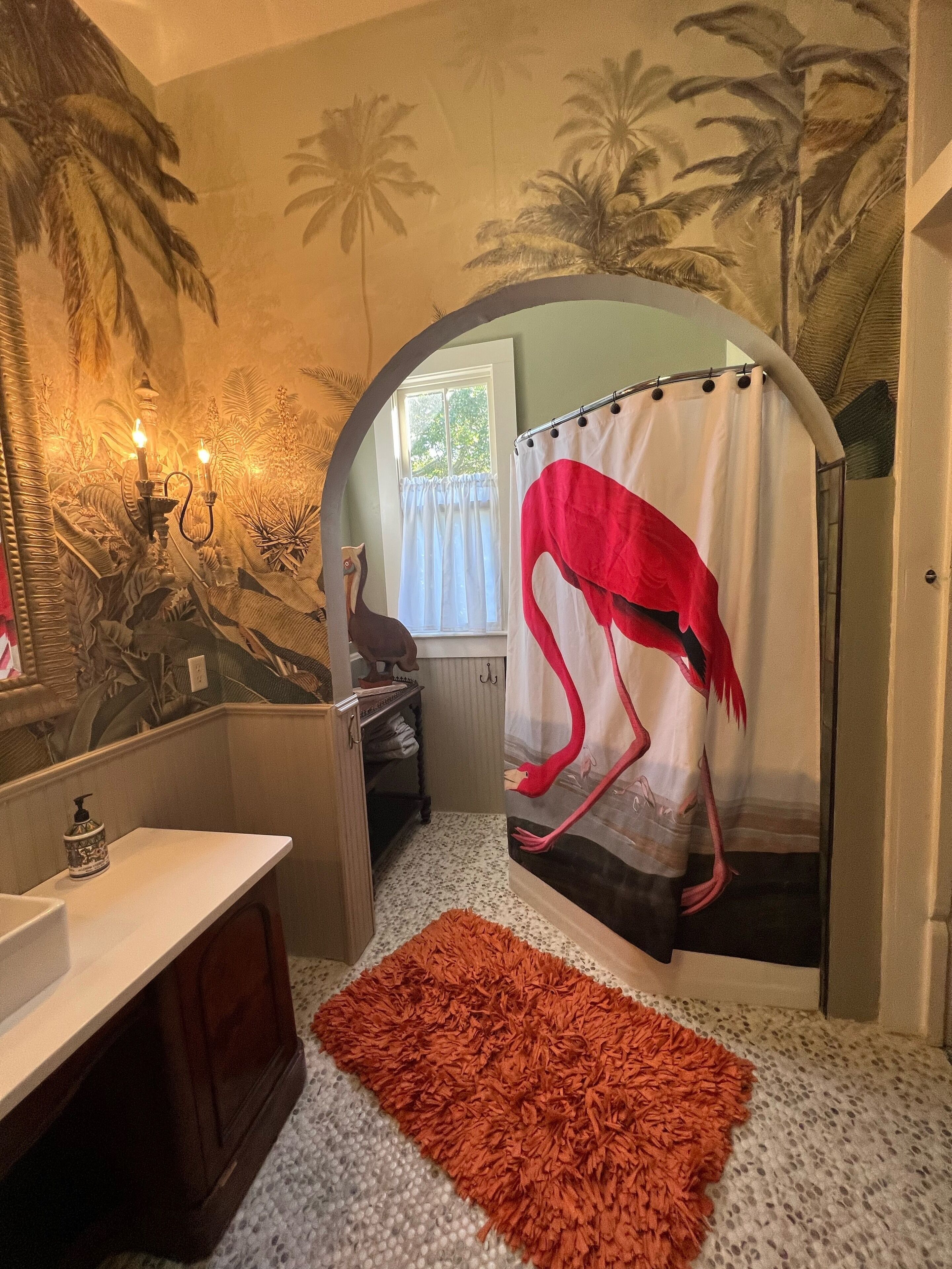 Un baño con cortina de ducha con diseño de flamenco, un lavabo blanco y un espejo.