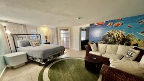 A bedroom with a bed, a sofa, a coffee table, and a painting of fish on the wall.