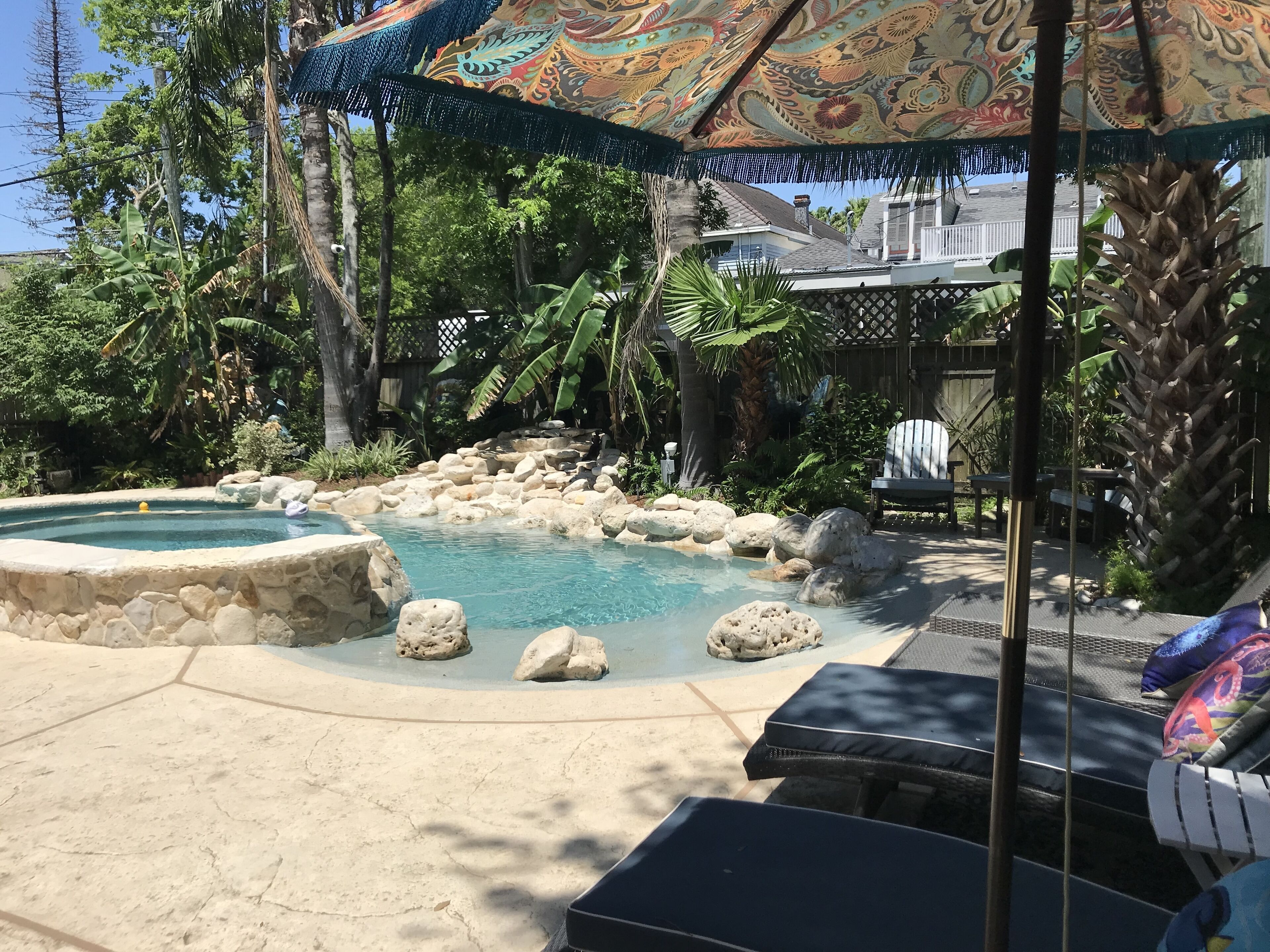 Un giardino con piscina, sedie a sdraio e un ombrellone in stile tiki.