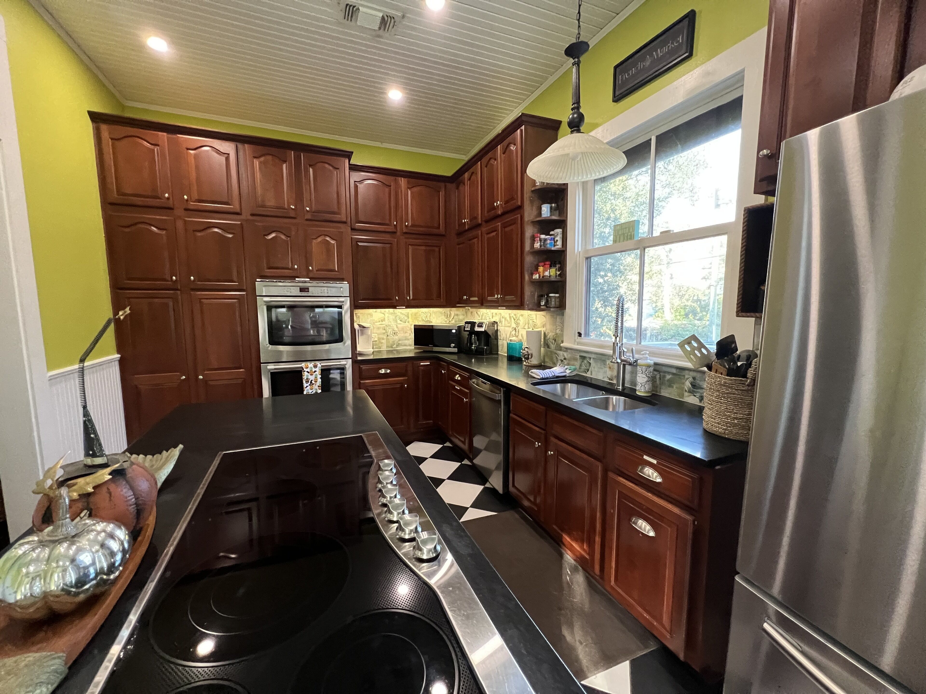 A kitchen with wooden cabinets, a stainless steel refrigerator, a microwave, and a large window.