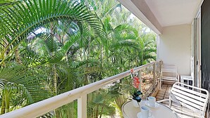 Un balcone con sedie in metallo bianco e un piccolo tavolo, circondato da rigogliosa vegetazione tropicale.