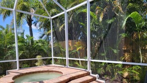 A hot tub with a brick surround and steps, surrounded by a glass enclosure with a view of dense tropical foliage. - Newer Upscale Home with Htd Pool & Spa - Bike or Walk to Beaches and Restaurants (Naples)