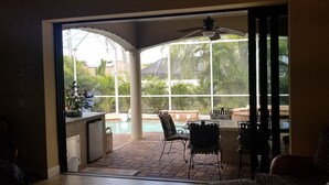 A room with a sliding glass door leading to a patio area with a pool, outdoor furniture, and a ceiling fan. - Newer Upscale Home with Htd Pool & Spa - Bike or Walk to Beaches and Restaurants (Naples)