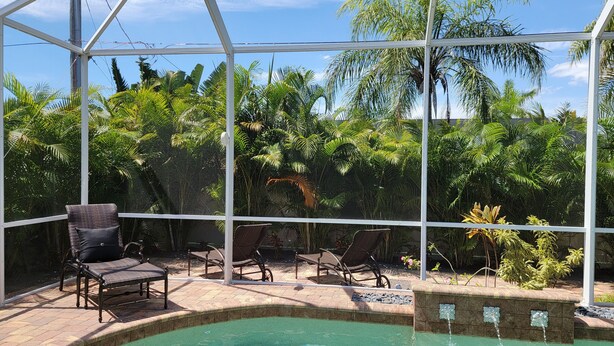 A pool area with a glass enclosure, lounge chairs, and tropical plants. - Newer Upscale Home with Htd Pool & Spa - Bike or Walk to Beaches and Restaurants (Naples)
