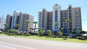 A multi-story hotel with a uniform facade, balconies, and a well-maintained lawn with palm trees. - 2BR 2 BA 5th floor beachfront condo. Call Now! (Gulf Shores)