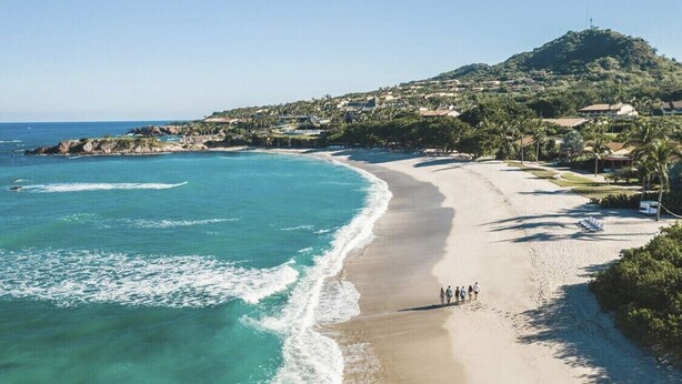 A beach with a clear view of the ocean and a hill with buildings in the background. - Ocean View Condo in Punta Mita, Beach Clubs access, Golf Cart, Breakfast, Pool. (PUNTA MITA)