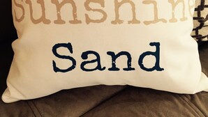 A pillow with the text "Surf Sunshine Sand" on it. - Apartment in the heart of Marquette w/ cable & wifi!!  Next to premier brewpub!! (Marquette)