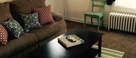 A living room with a brown sofa, a black coffee table, a green chair, and a striped rug.