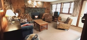 Una sala de estar acogedora con chimenea de piedra, un sofá azul, sillones estampados y una mesa de centro de madera.