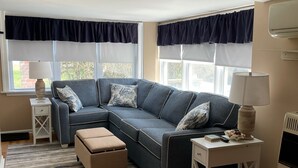 A modern living room with a sectional sofa, a small ottoman, a side table with a lamp, and a radiator.