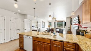 Una cocina con encimeras de granito, armarios de madera e iluminación colgante.