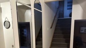 Une pièce dotée d’un plancher en bois, d’un escalier et d’un grand miroir qui reflète l’intérieur.