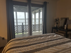 Ein Schlafzimmer mit einem großen Bett, Blick auf einen Balkon mit Gittergeländer sowie eine Kommode mit Spiegel und Blumen.