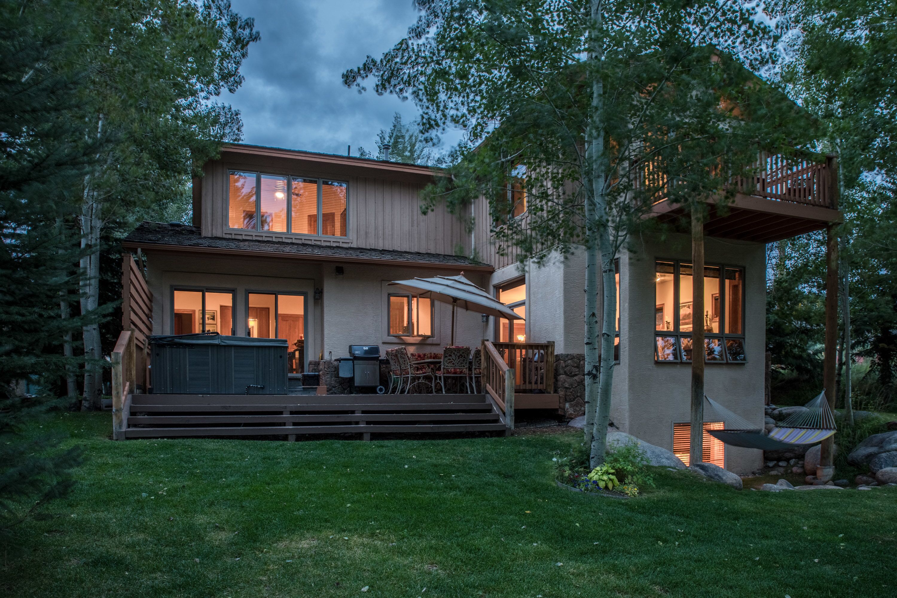A two-story house with a deck, outdoor seating, and a hammock.