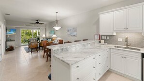 A modern kitchen with white cabinetry, a marble island, and a large window overlooking a garden. - Walking Distance to Snook Inn, Smith House, Shopping, Day Spa & Live Music! (Marco Island)