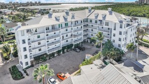 A multi-story hotel with a central courtyard, surrounded by greenery and a view of a body of water. - Walking Distance to Snook Inn, Smith House, Shopping, Day Spa & Live Music! (Marco Island)