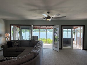 Ein Wohnzimmer mit einer großen, grauen Couch, einem Deckenventilator und Blick auf einen See durch offene Türen.