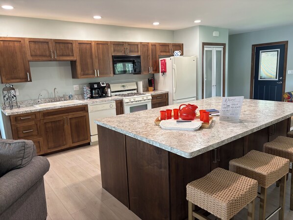 Eine moderne Küche mit Holzausstattung, einer Granit Arbeitsplatte, einem Edelstahlbackofen, einer Mikrowelle, einem Kühlschrank und einer Bar mit Barhocker.