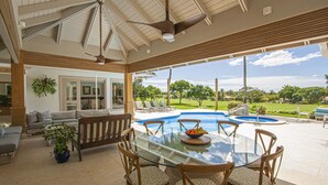 A covered outdoor area with a glass table, chairs, and a pool. - ATTRACTIVE RATES JUST REMODELED  - Near Beach 4 BD Amazing Golf View Villa (La Romana)