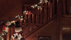 A cozy room with a wooden staircase, a Christmas tree, and a television displaying a scene. -  Decorated for Country Christmas 2 BR & 2 BA Loft Crib & Highchair Wi-Fi no pets (Pigeon Forge)