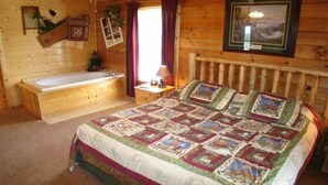 A wooden cabin bedroom with a large bed, a wooden headboard, a window with curtains, a wooden bench, and a small table with a lamp. -  Decorated for Country Christmas 2 BR & 2 BA Loft Crib & Highchair Wi-Fi no pets (Pigeon Forge)