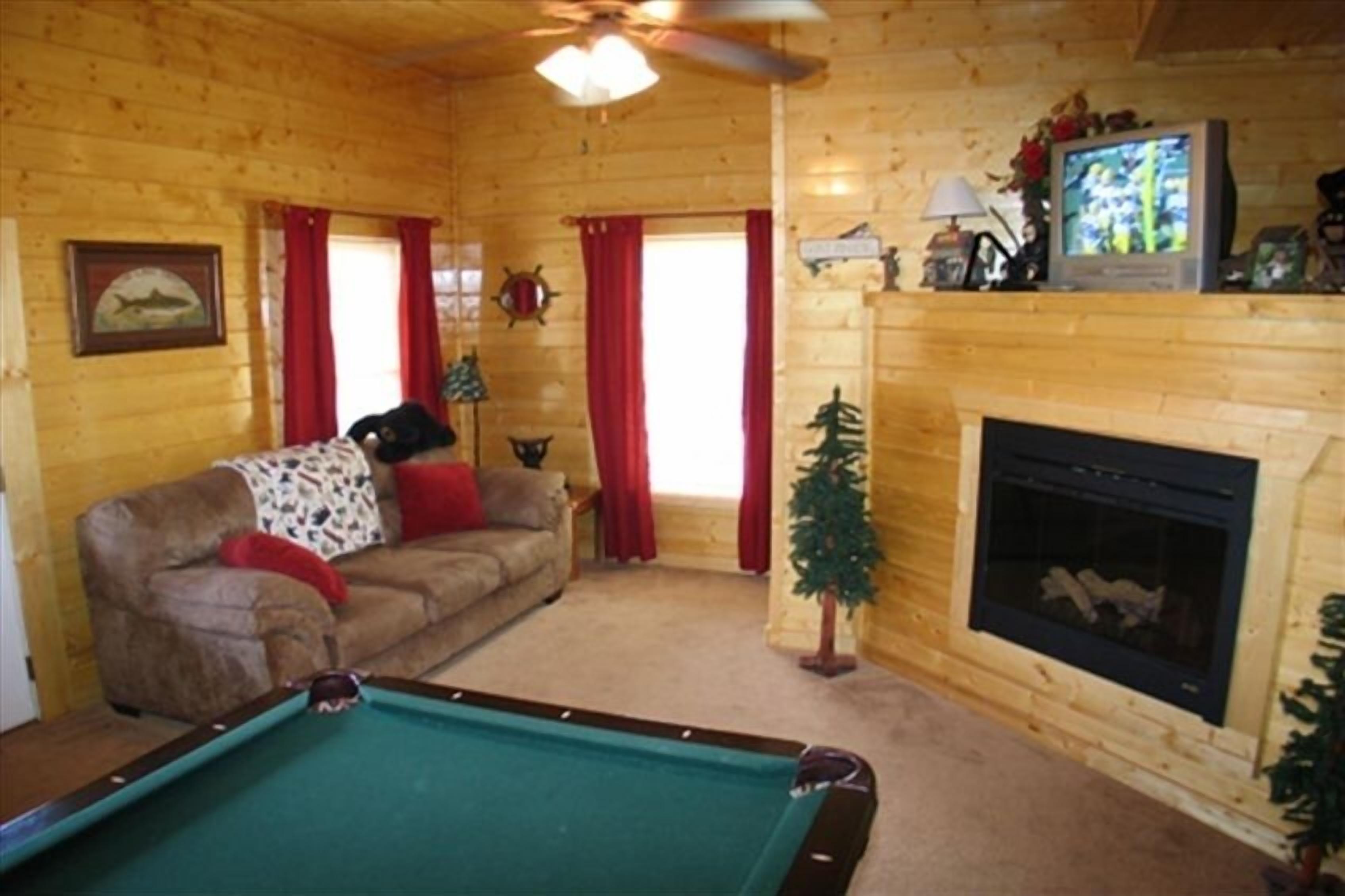 A cozy cabin interior with a pool table, a fireplace, and a television.