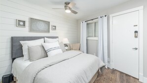 Une chambre à coucher avec un lit, une table de chevet, un ventilateur de plafond et une porte.