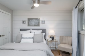 A bedroom with a bed, a nightstand, a chair, a ceiling fan, and wall-mounted lamps.
