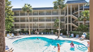 Un hôtel doté d’une piscine entourée de chaises longues et de palmiers.