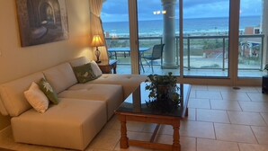 A living room with a sofa, a glass coffee table, and a view of the ocean through large windows. - Sept Special: 7 nights just 1229 plus resort fees.  Great view & location (Pensacola Beach)