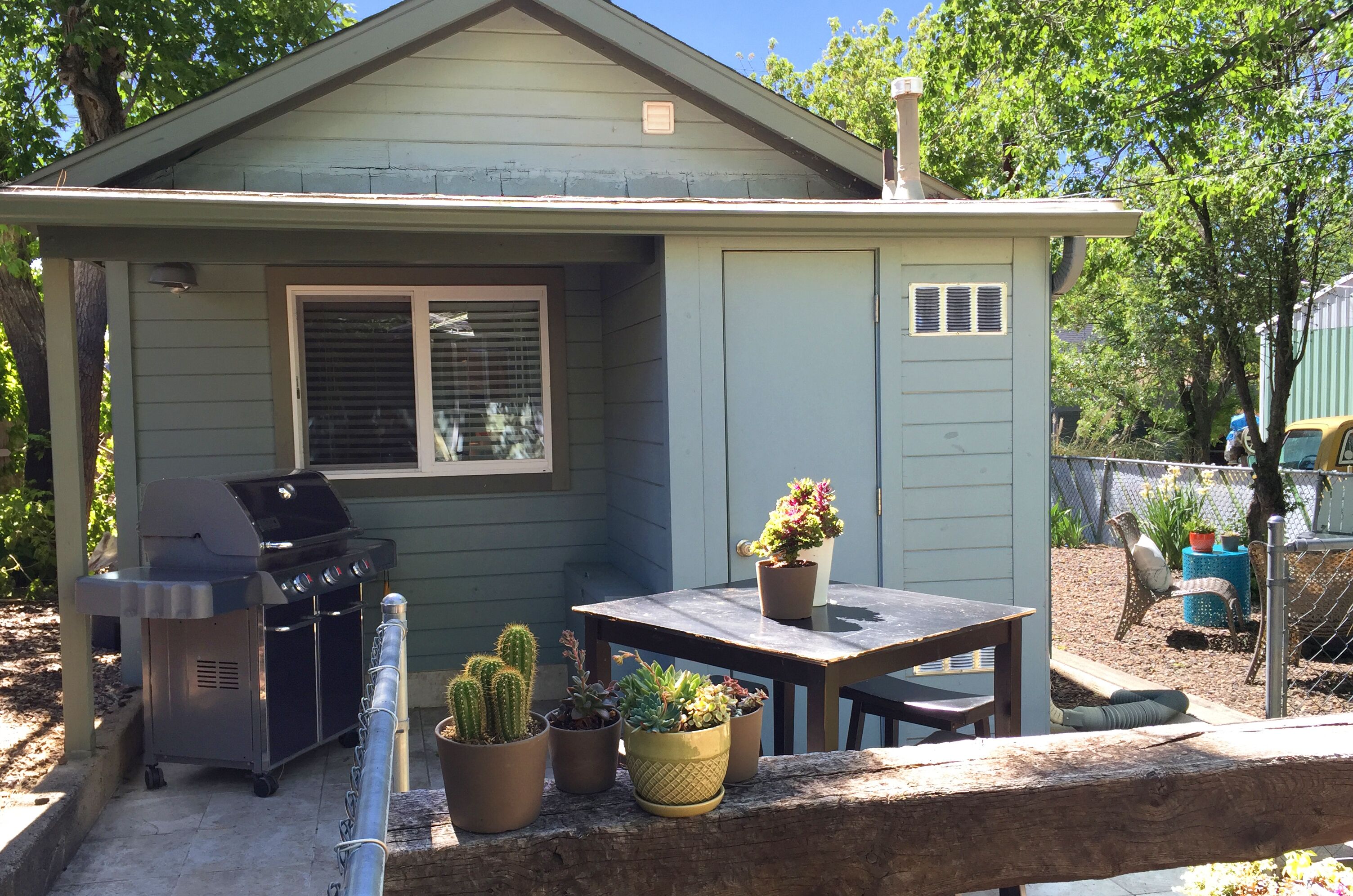 Et lille hus med en patio, grill, bord og plantekasser.