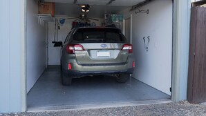 En Subaru Outback holder parkeret i en garage med en ventilator i loftet og en dør til højre.