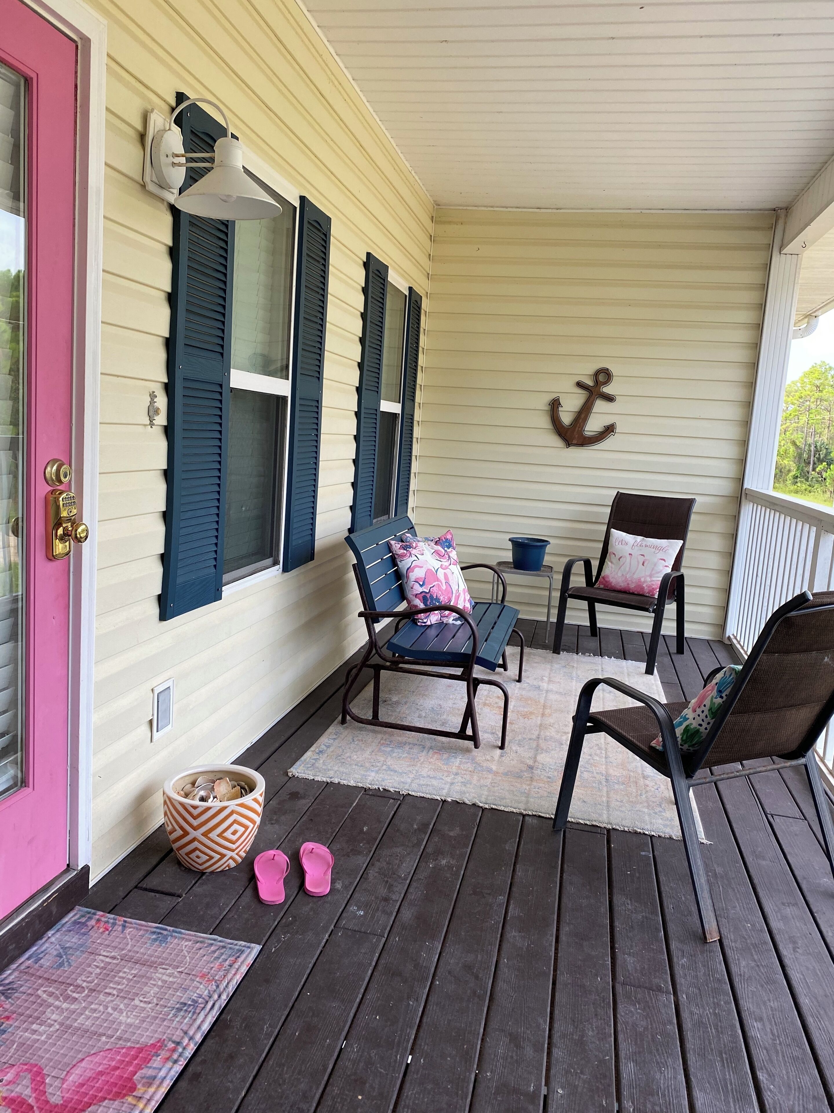 A covered porch with two chairs, a small table, and a decorative anchor on the wall.