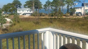 A coastal view from a balcony with a white railing, overlooking a grassy area with trees and a body of water.
