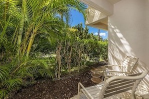 A patio with a white chair, surrounded by lush greenery and a clear blue sky.