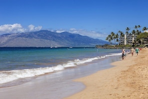 A beach with clear blue water, a sandy shore, and a mountain in the background.