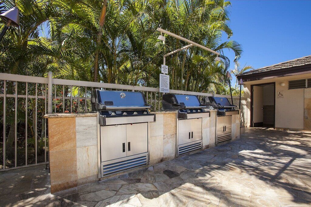 A row of barbecue grills with a stone wall and a metal fence in the background.