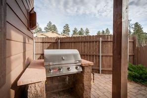 A gas grill with four burners, a side shelf, and a chimney.