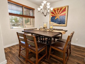 A dining room with a wooden table and chairs, a chandelier, a window with blinds, and a painting on the wall. - Relax in the Pines at the Flagstaff Base Camp (Flagstaff)