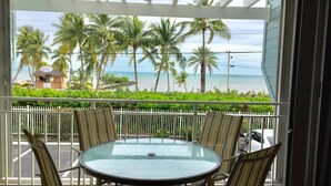 A covered outdoor area with a glass table and striped chairs, overlooking a beach with palm trees and a small building labeled "Sunshine Motorsports". - GATED OCEANFRONT CONDO AT SMATHER'S BEACH (Key West)