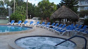 A swimming pool with lounge chairs, a hot tub, and a thatched-roof structure. - GATED OCEANFRONT CONDO AT SMATHER'S BEACH (Key West)