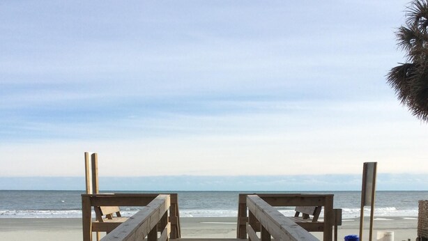 Eine Holzpromenade führt zu einem Strand mit freiem Blick auf das Meer.