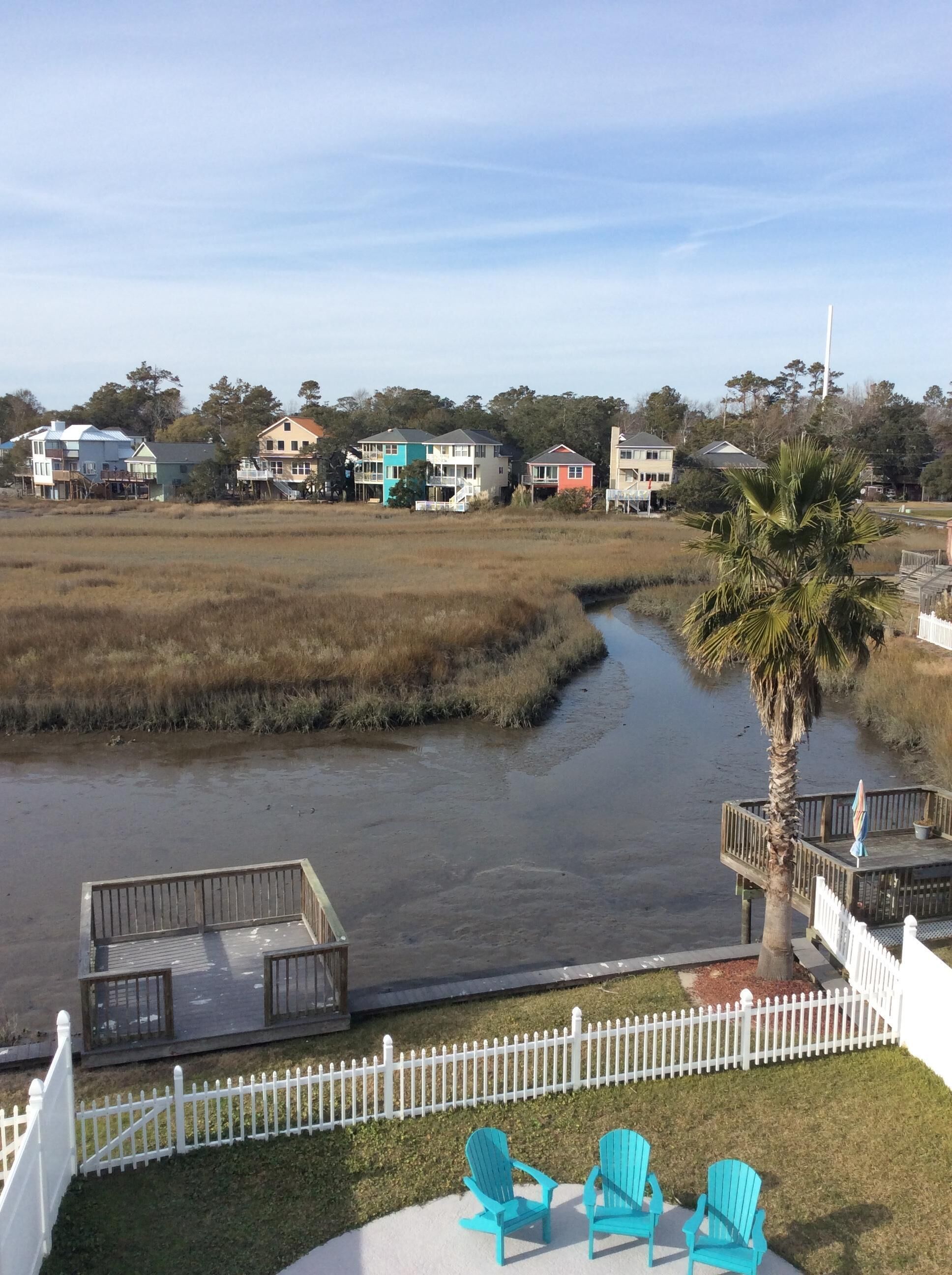 A view of a waterfront property with a wooden deck, two turquoise Adirondack chairs, and a white picket fence.