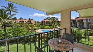 Un balcon avec une table ronde et des chaises, donnant sur une piscine et une végétation luxuriante.