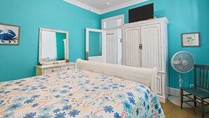 Un dormitorio con cama, cómoda, armario, ventilador y una silla.