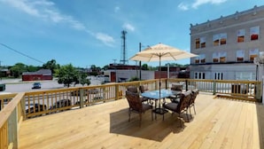 Una terraza de madera con una mesa y sillas, una barandilla amarilla y un edificio al fondo.